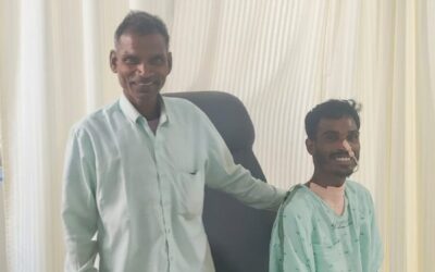 Two men in the new ICU at Chinchpada Christian Hospital. One man, Lakhan, is in a hospital gown and has tubes attached to him. The other man, Lakhan's father, is smartly dressed. They are both smiling.